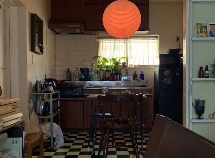 ダークブラウンの家具とモノトーンの市松模様の床が特徴的なアパートのキッチン、暖色のペンダントライトを配した印象的な空間