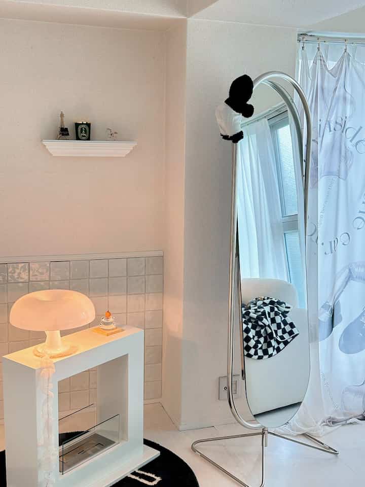 White and silver toned living room featuring a standing mirror and table lamp with a minimal and clean atmosphere