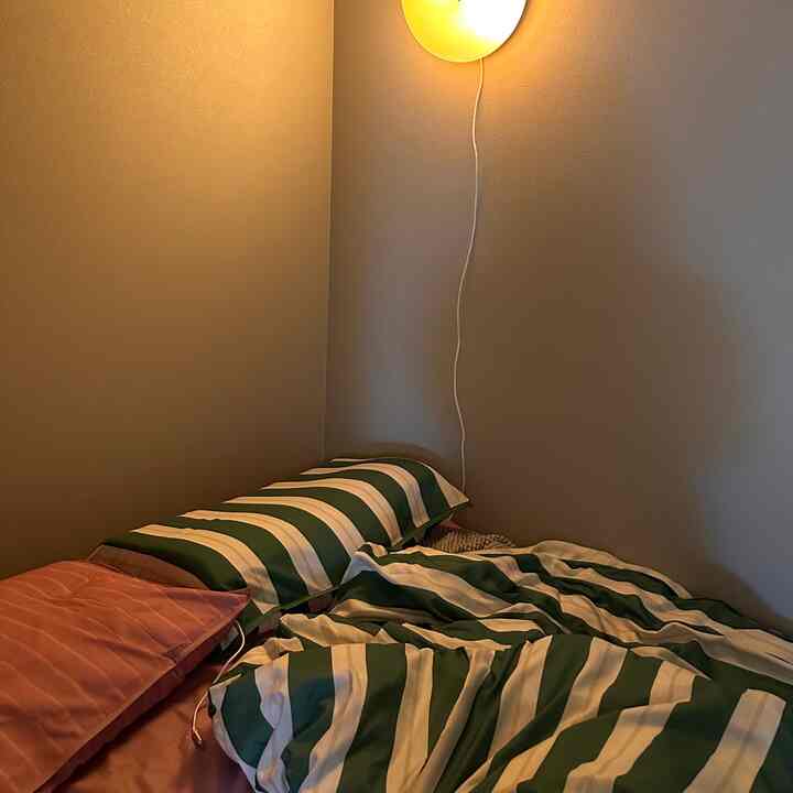 ベージュの壁と緑白のストライプの寝具が配置された温かみのある寝室のインテリア。