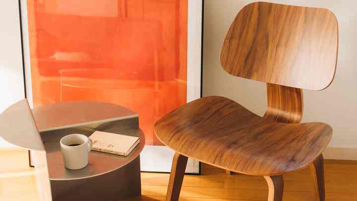 温かみのあるナチュラルな色調のリビング、木製アームチェアとシルバーのサイドテーブル、オレンジ色の額縁が配置された雰囲気のあるインテリア