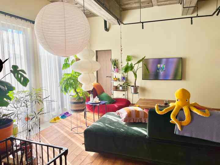 Natural toned living room featuring a dark green sofa, red armchair, lush plants, and round Japanese-style paper lanterns creating a bright atmosphere