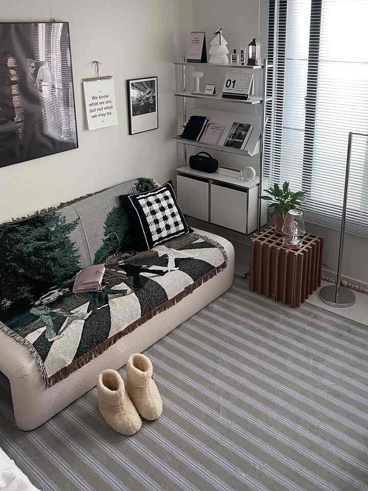 白とグレーのトーンが特徴のコンパクトなリビング、モダンなソファとフロアランプ、壁アートと植物が配置された雰囲気のあるインテリア