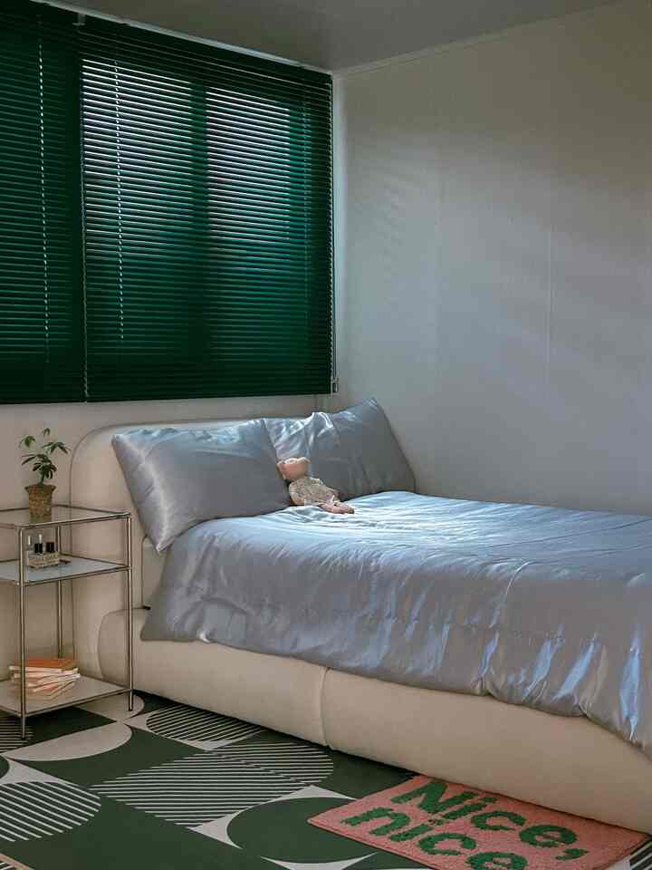 Calm white and green toned bedroom featuring a minimal bed, metal nightstand, and geometric patterned rug in a harmonious space