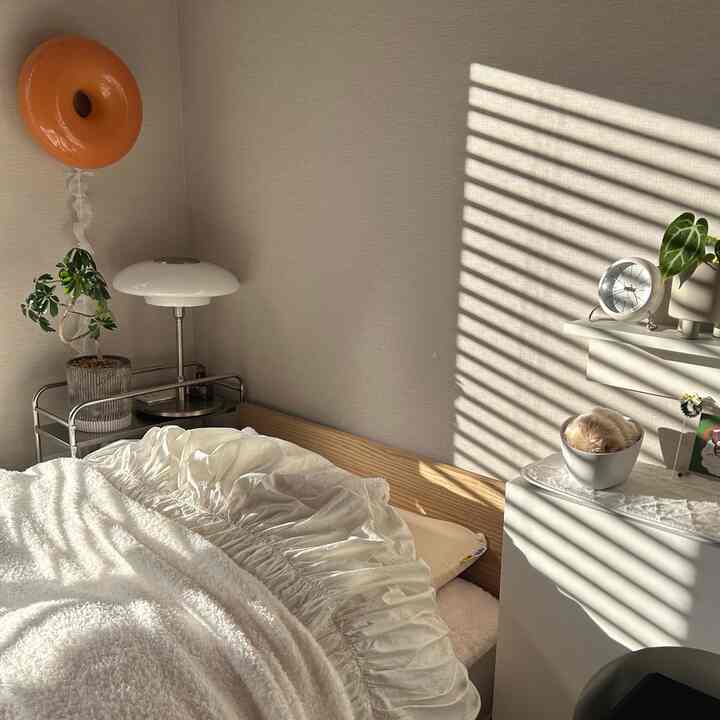 ベージュとホワイトの色調の寝室、ベッドとナイトテーブルが配置され、柔らかな自然光が漂う落ち着いたインテリア