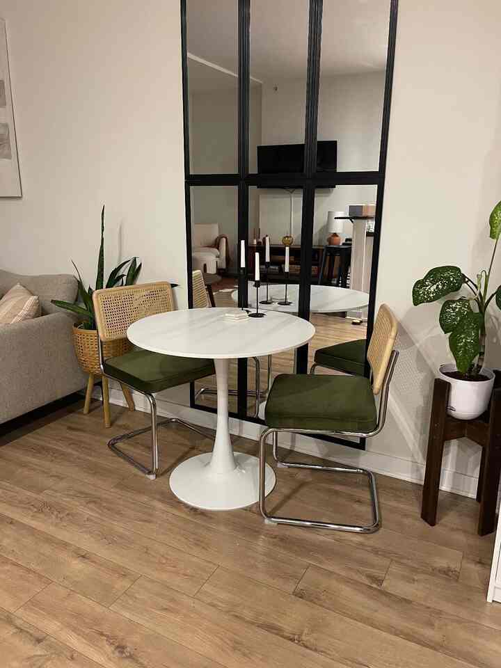 Natural-toned wood flooring dining room featuring white tulip table and green cushioned chairs with cozy atmosphere