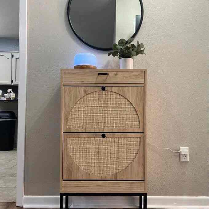 Natural-toned entrance space featuring a Scandinavian style rattan front sideboard, round mirror and blue light diffuser on a minimalist backdrop