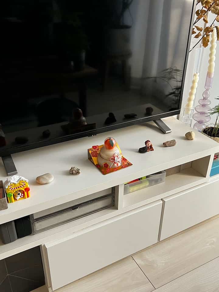 White-toned living room featuring a corner-style white TV stand with decor items in the center, showcasing a simple interior design