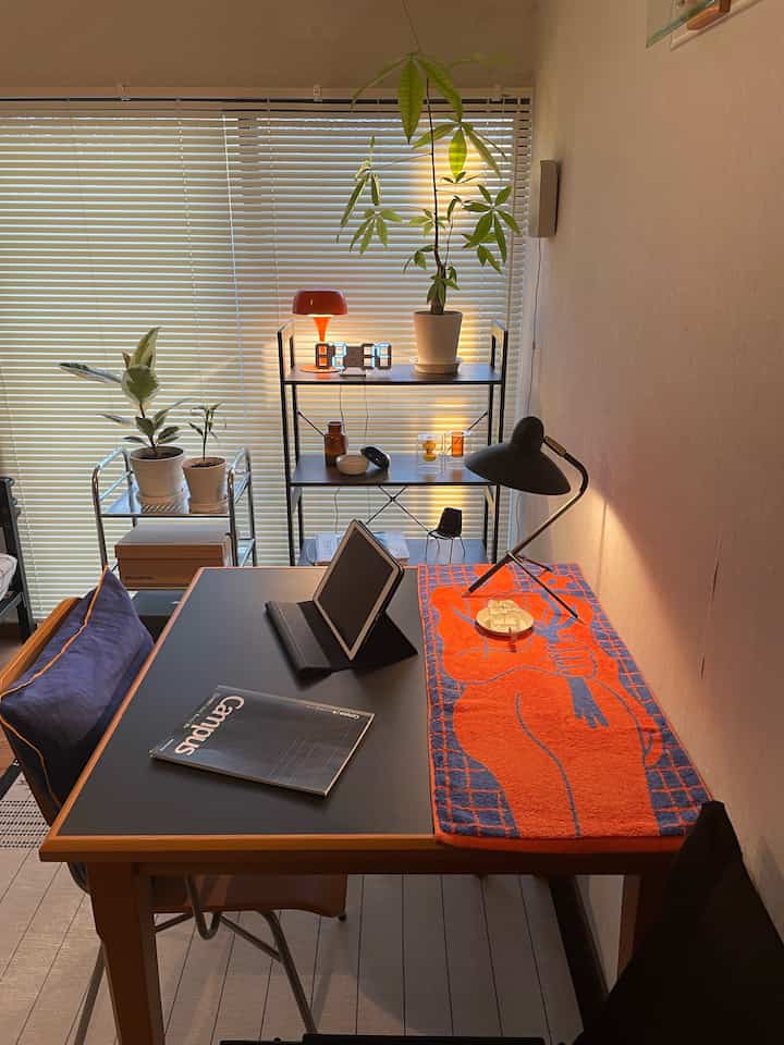 ブラックと木目調の調和が美しいダイニングルーム、鮮やかなオレンジのテーブルランナーとテーブルランプが配置されたモダンで雰囲気のあるホームオフィス空間