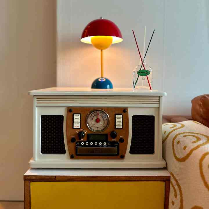 Living room with dominant red, yellow, blue colors and wood tones, featuring a white nightstand, colorful table lamp, and cozy throw blanket