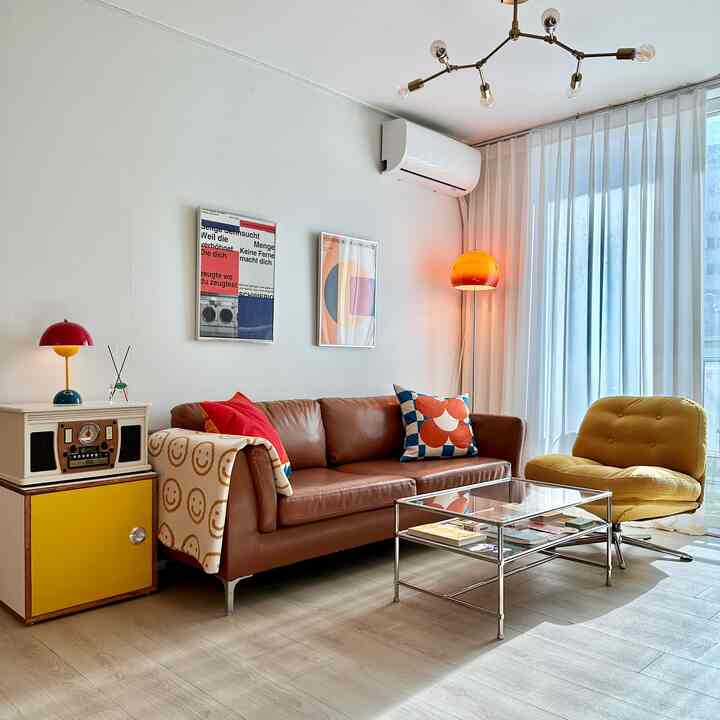 暖色のミッドセンチュリーモダンリビング、レザーソファと黄色のアームチェア、ガラスのコーヒーテーブルが配置された印象的な空間