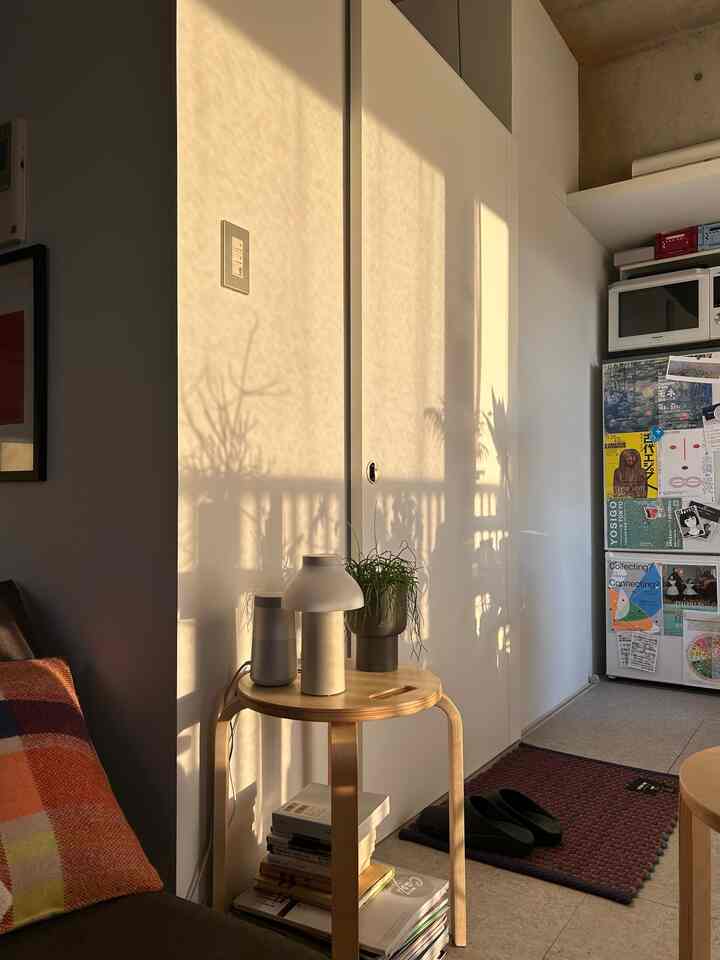 Warmly lit white studio apartment featuring a natural wood stool and potted plants with cozy ambiance