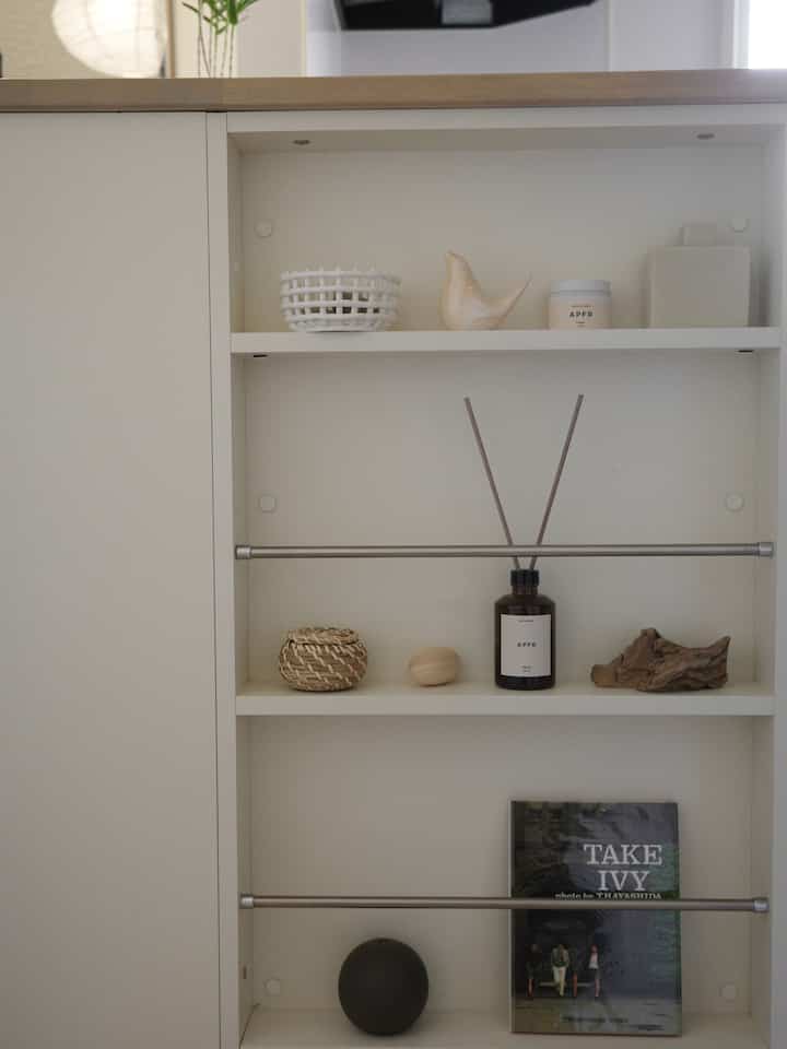 白を基調としたキッチン横のディスプレイラック、木のオブジェが配置されたシンプルで清潔感のあるインテリア