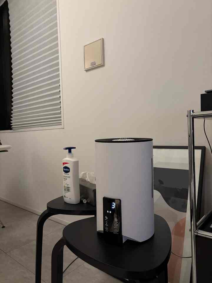 White-toned living space featuring a white cylindrical humidifier centrally placed on black stools with a minimalistic feel