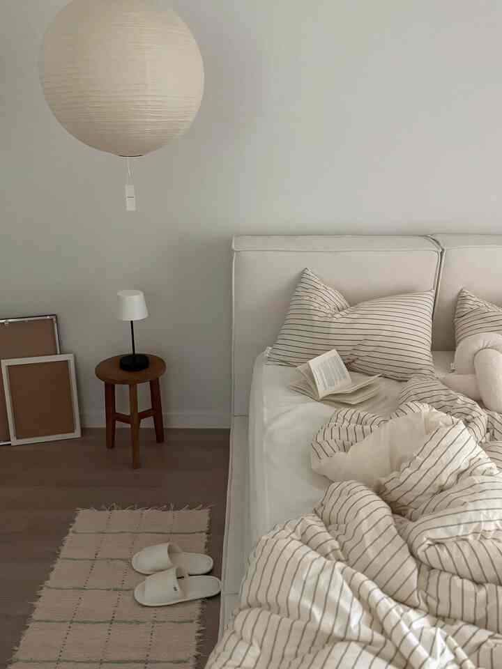 ホワイトとベージュの色調の寝室、シンプルなベッドフレームとストライプの寝具が配置された印象的な空間