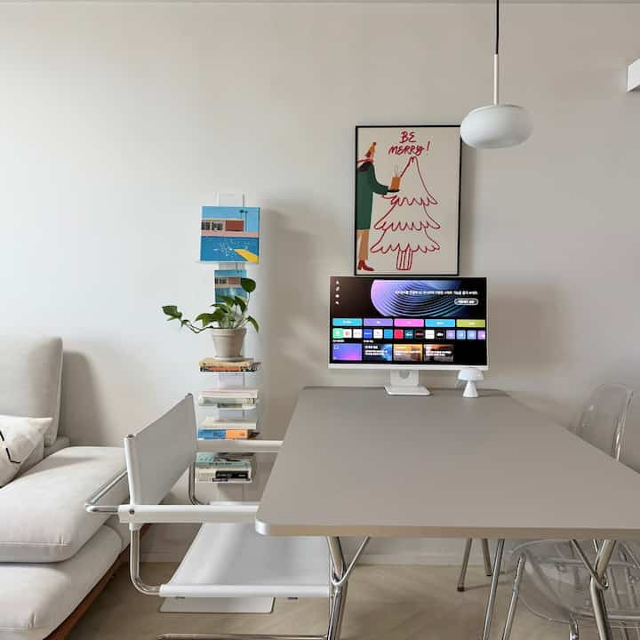 A white and gray toned home office and dining space featuring a modern dining table, chairs, monitor, and vintage framed art in a neat interior