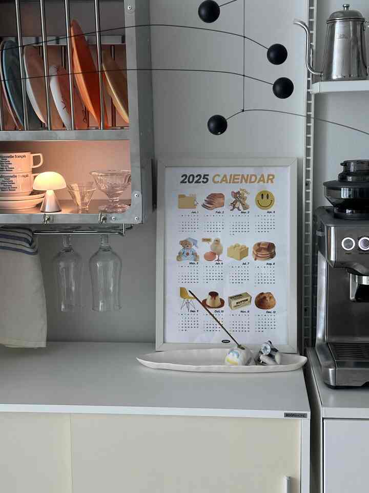 White-toned kitchen space featuring a poster calendar for 2025 on the storage cabinet and an espresso machine for a neat home cafe setup