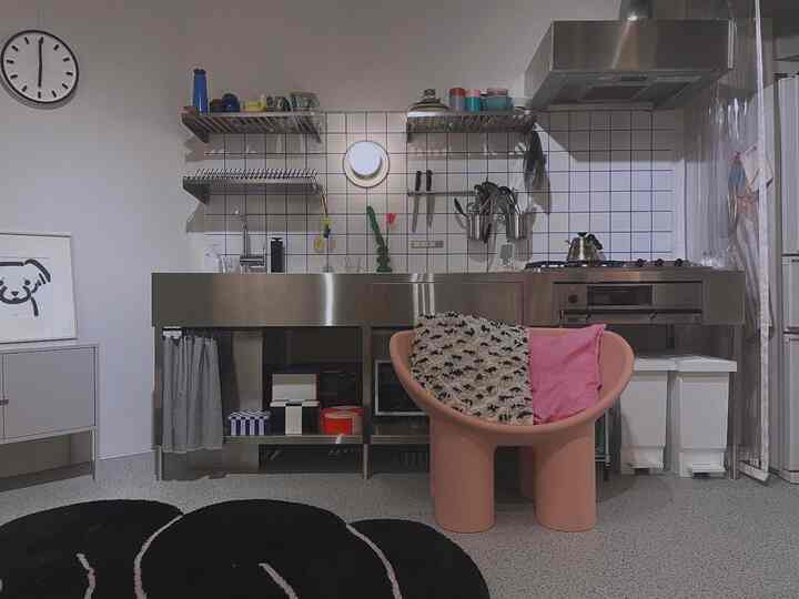 白とステンレスの色調のモダンなキッチン、ピンクのアームチェアが配置された印象的なインテリア