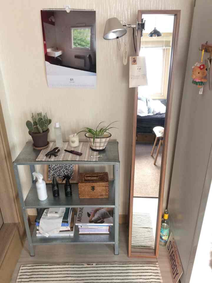 ベージュとグレー調のコンパクトなワンルーム、金属製3段シェルフと全身鏡が配置された実用的な空間