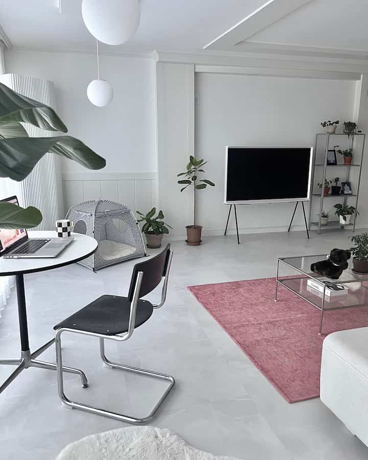 A modern living room dominated by white and black tones featuring a pink rug and a pet tent, creating a clean and cozy ambiance