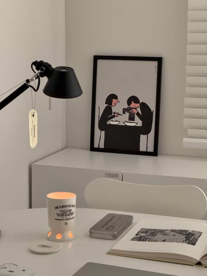 ホワイトトーンのシンプルでモダンなホームオフィス空間、黒いテーブルランプとアートフレームが配された整ったデスク環境