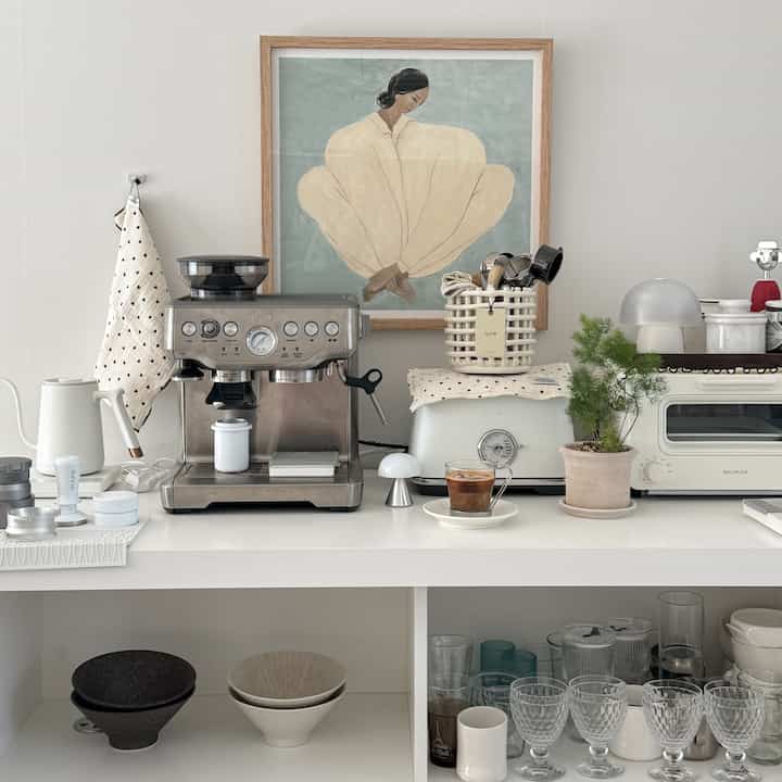White and gray toned kitchen home cafe space featuring coffee machine and cabinet with neatly arranged dishes in a minimalistic interior