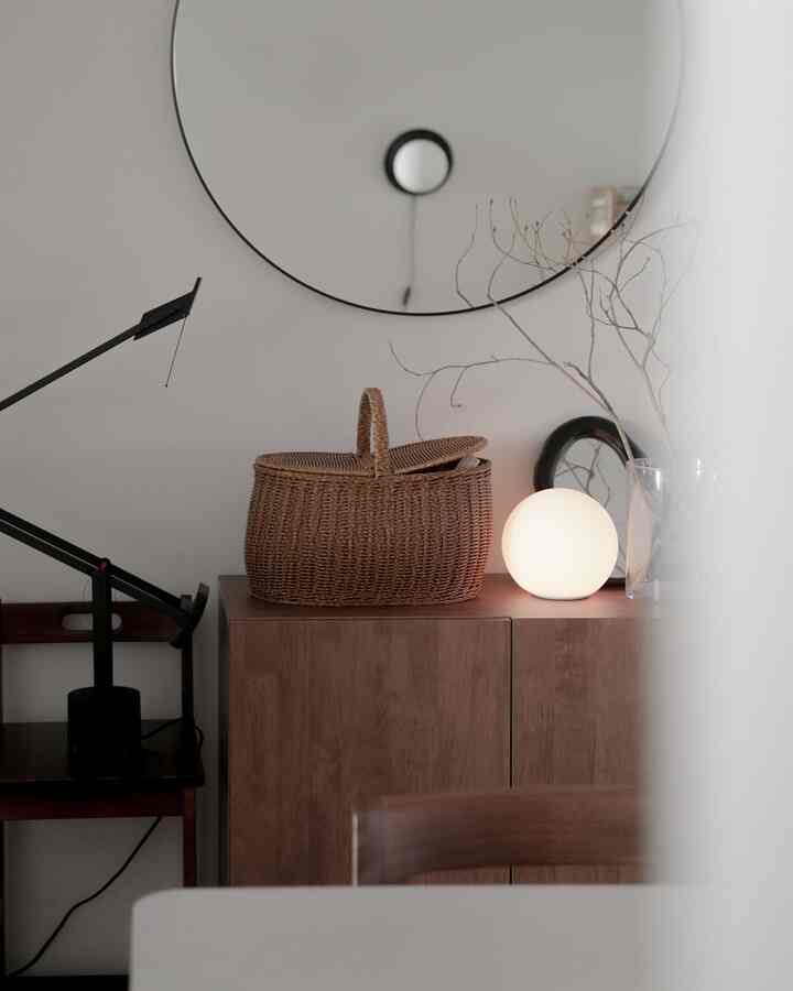 Natural wood tones and white walls define the entrance area featuring a round mirror, rattan basket, and Artemide lamp creating a cozy atmosphere