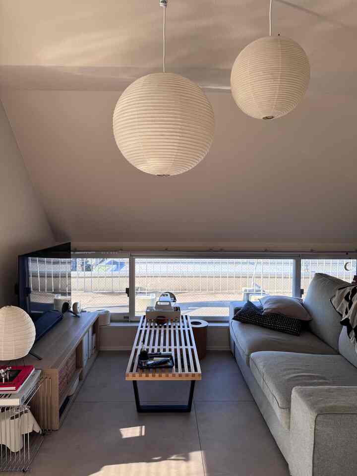 Beige-toned living room featuring gray sofa, wooden coffee table, and Japanese-style pendant lamps creating a cozy atmosphere