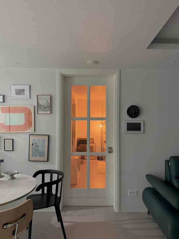 Modern living room with white walls and black accents, featuring an Arne Jacobsen wall clock and framed pictures in a simple interior