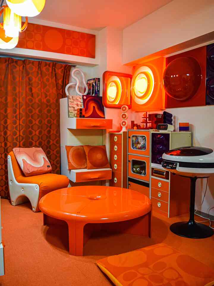 オレンジ色調のレトロなリビング、ユニークなミッドセンチュリーモダン家具とペンダントライトが配置された温かみのある雰囲気のインテリア