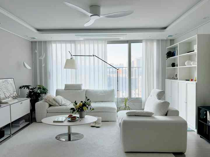 Monotone white living room featuring two sofas, a coffee table, rug, and plants creating a clean and cozy atmosphere