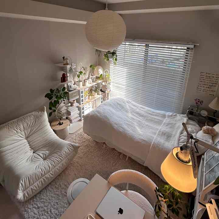 白とナチュラルカラーの8畳ワンルーム、ラウンジチェアとデスク、多数の植物が配置された落ち着いたインテリア