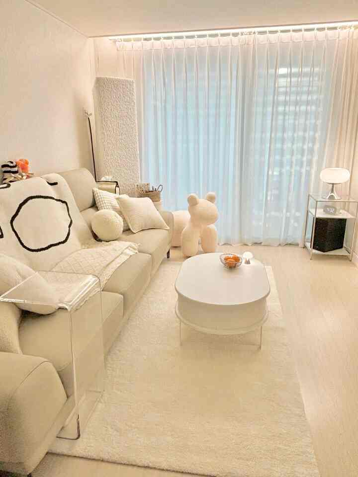 明るく白を基調としたリビング、ベージュのソファとシアーカーテン、シンプルな丸いテーブルが配置された落ち着いた雰囲気のインテリア