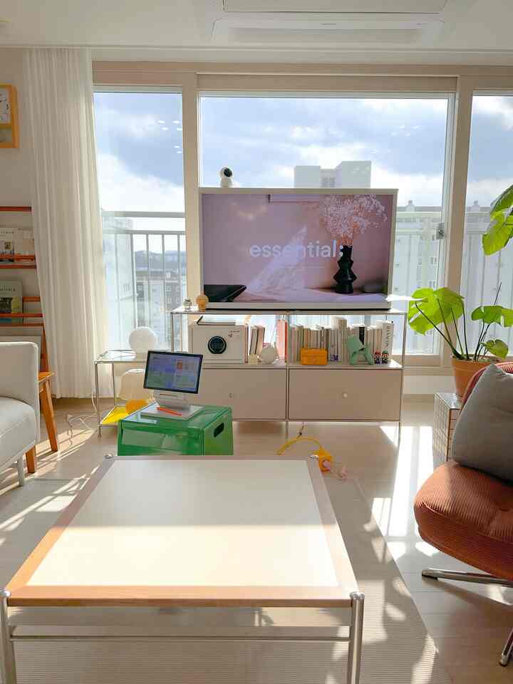 明るいホワイトとナチュラルカラーのリビング、中央にテレビ台とテーブル、右側に大きな植物が配置された温かみのある雰囲気の空間