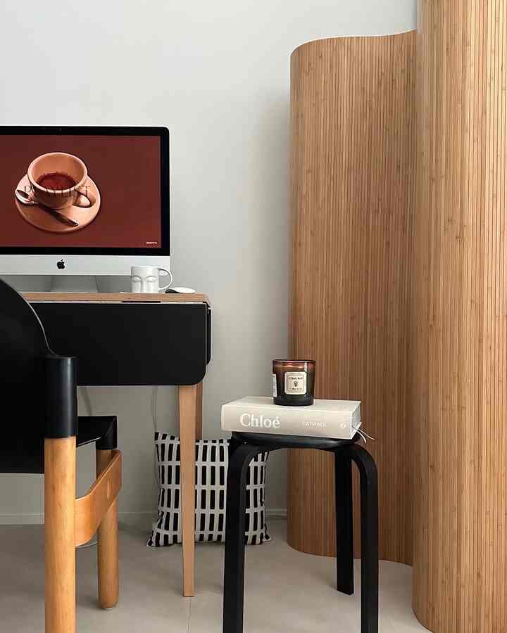 Modern study with wood tone room divider and black stool, featuring a clean and minimal home office setup