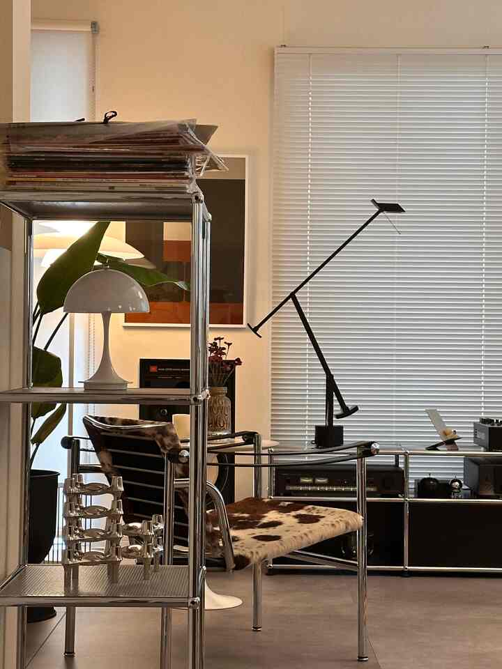 Silver metallic tone living room featuring a mid-sized armchair, USM Haller shelving, table lamp, and blinds in a modern interior.