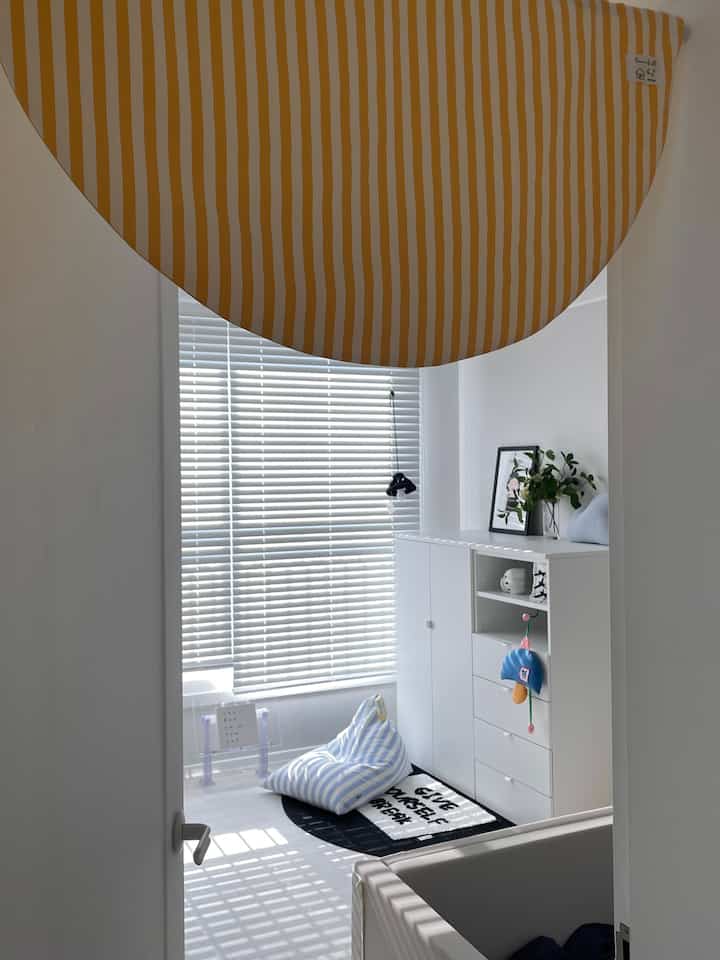 ホワイトの壁と床に収納家具が配置され、ストライプのビーズクッションとブラインドが調和した明るく清潔感のあるナチュラルモダンなインテリア