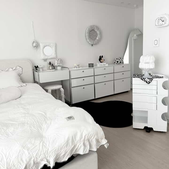 Modern bedroom in white and black tones featuring a frilled bedding set, multi-storage drawers, and a contrasting rug in a tidy atmosphere