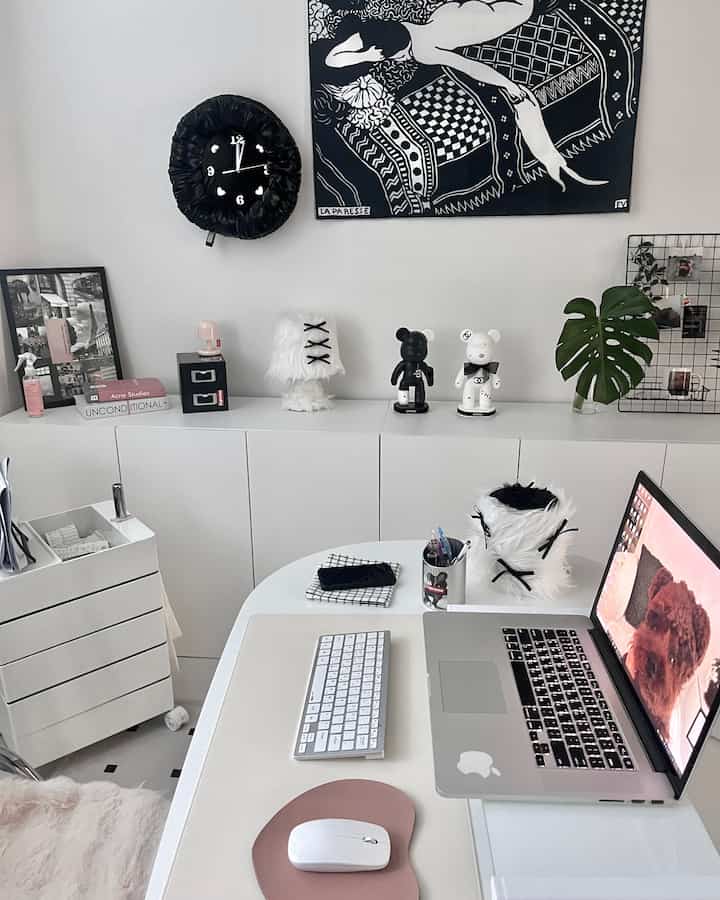 Modern home office in white and black tones featuring a desk, monitor stand, and drawer cabinet arranged neatly