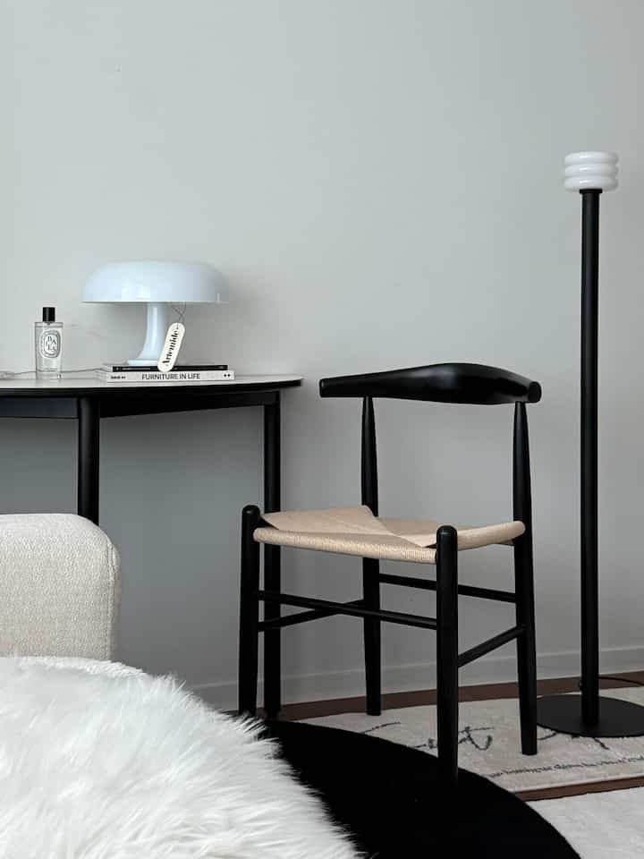 Monotone living room featuring a natural wood rattan chair, black side table, and floor lamp in a clean and stylish setting