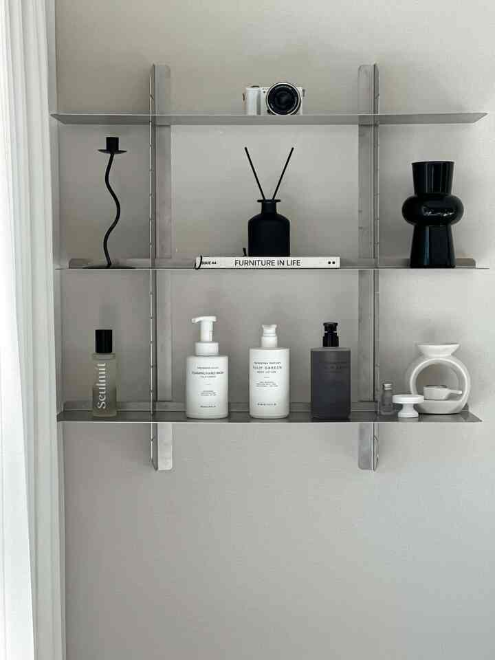 Modern bathroom space with metal shelf holding black and white items against white wall and curtain background