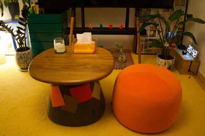Warm orange-toned living room featuring a wooden living table and a bright orange ottoman, creating a cozy and colorful atmosphere
