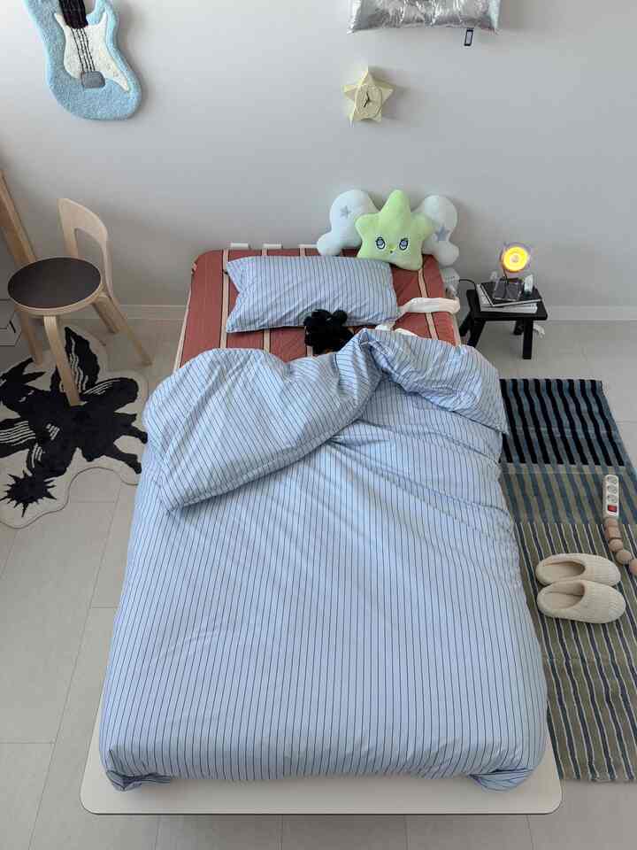 白と青のトーンでまとめられた6畳の寝室、ストライプの寝具と小さなスツール、ラグが配置された雰囲気のある睡眠スペース