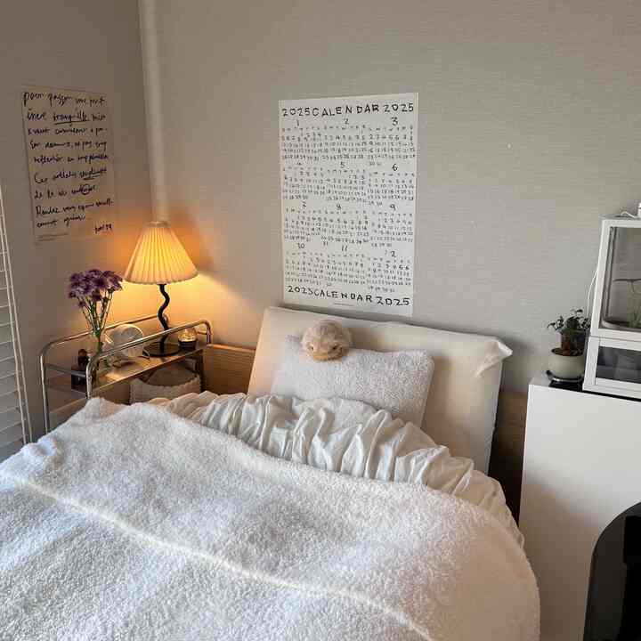 Cozy bedroom in warm brown and white tones, featuring ivory bedding and soft table lamp lighting