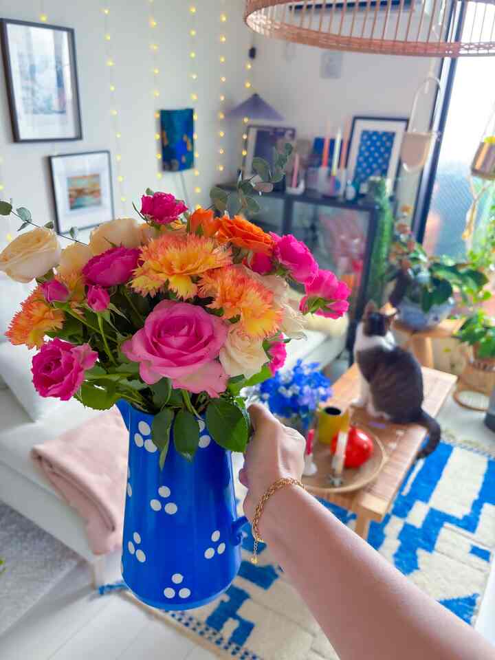 鮮やかな花が青い花瓶に生けられたナチュラルなリビングルーム、白いソファと木製のコーヒーテーブルに猫が座る落ち着いた空間