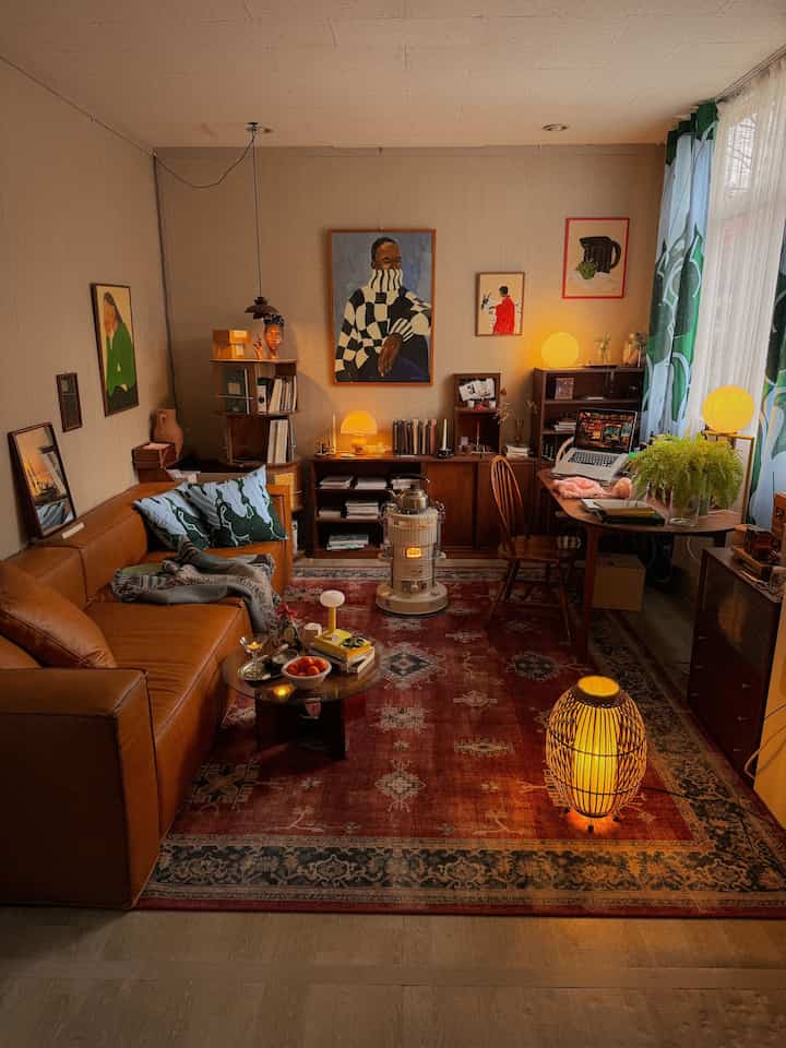 暖かいブラウンの木目調と照明が調和したワンルームのリビング、レザーソファと本棚、デスクが居心地の良い雰囲気を演出するインテリア