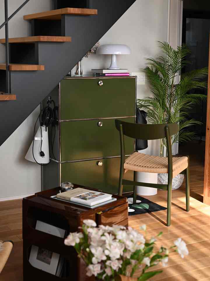 A mid-century modern cozy space featuring natural wood tones, olive green cabinet and chair placed under the stairs