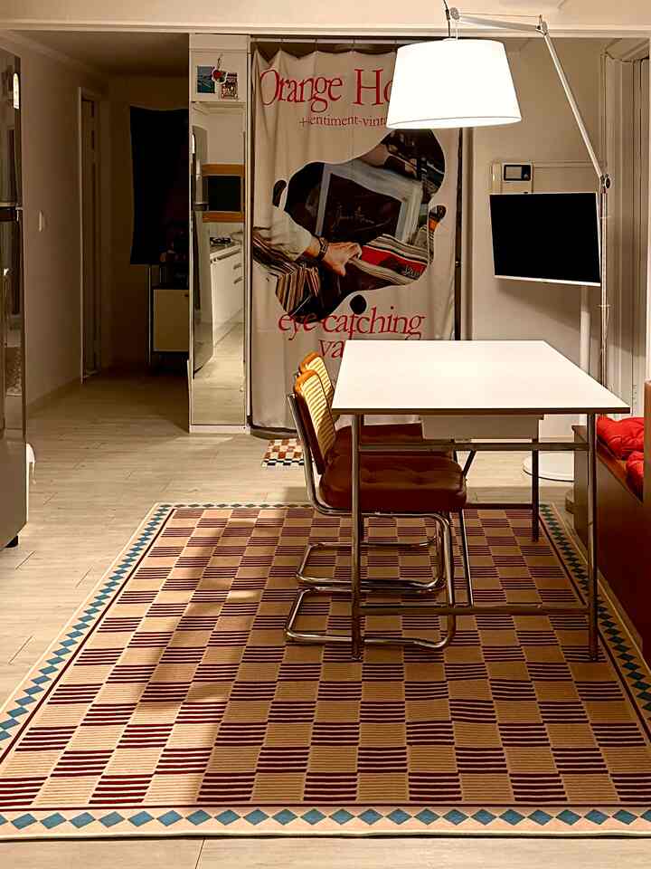 オレンジとブラウンの色調が広がるリビング兼ダイニングルーム、白いテーブルと大きなヴィンテージラグが調和する雰囲気のあるインテリア