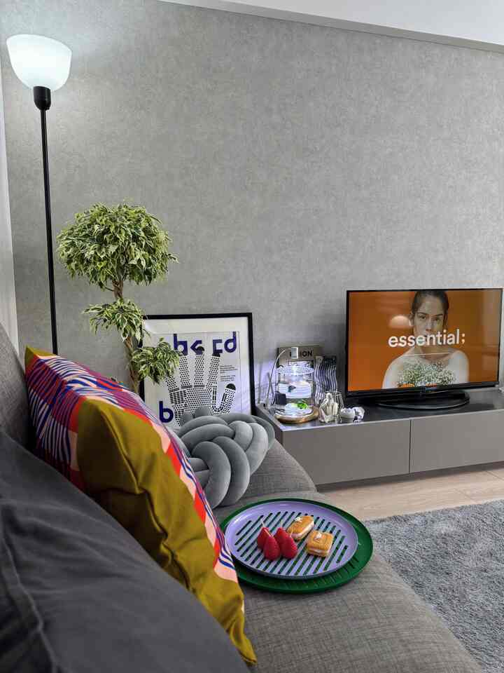 グレーの壁とソファが配置されたモダンなリビング、グリーン植物とフロアランプがアクセントの雰囲気あるインテリア