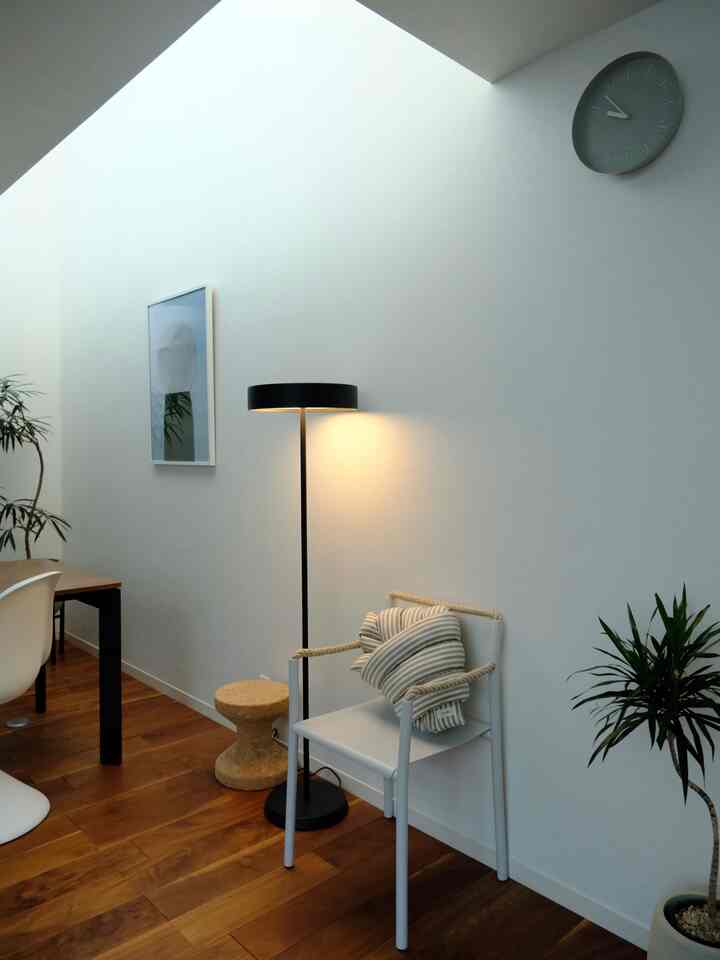Mid-Century Modern living room with white walls and wood-toned floor, featuring a floor lamp and cork stool in a simple, warm atmosphere