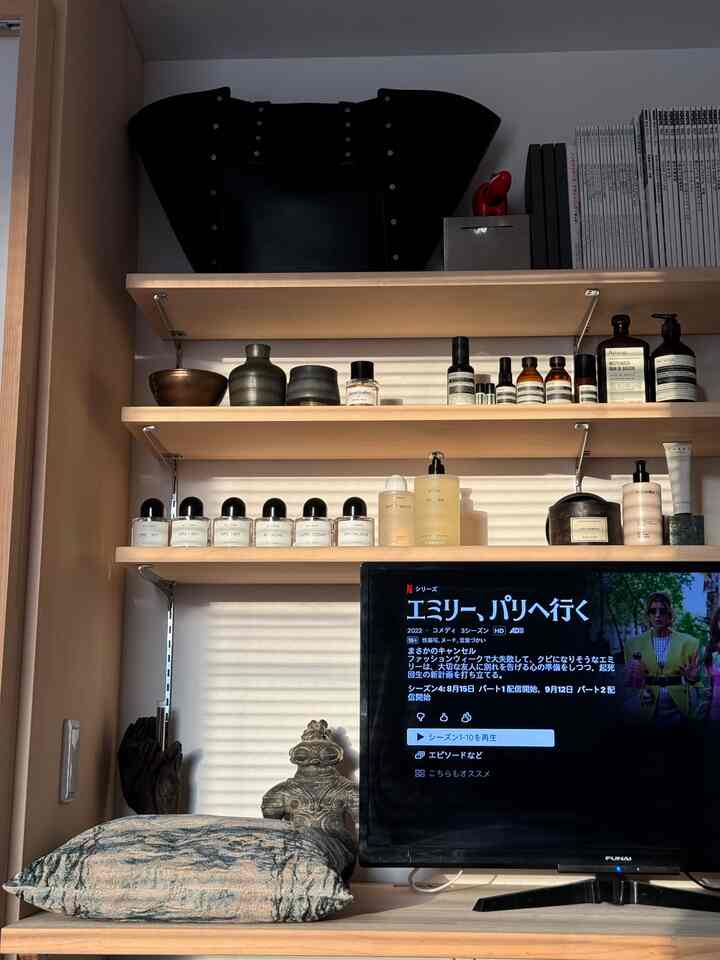 温かみのある木目調と黒を基調とした一人暮らしのリビング、テレビ台と多様なディフューザーや化粧台のアイテムが配置された落ち着いたインテリア